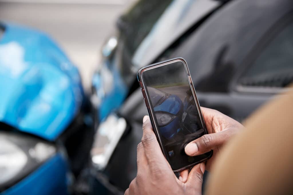 male motorist involved in car accident taking picture of damage for insurance claim